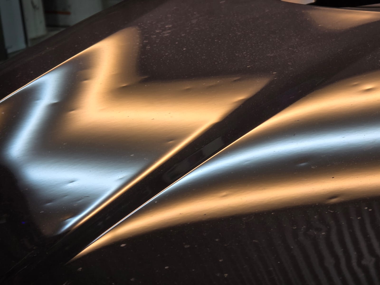 Hail damage on car roof showing dents under light